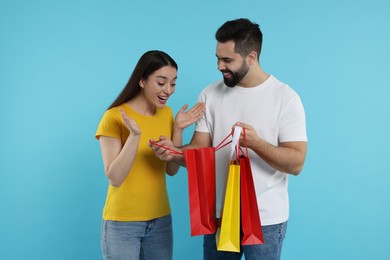Photo of Man showing shopping bag with purchase to his excited girlfriend on light blue background