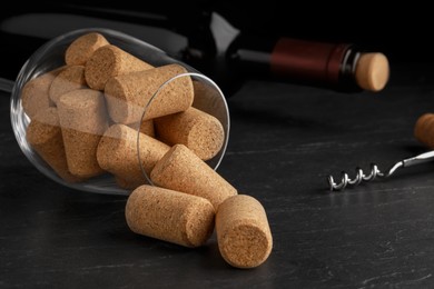 Glass with wine corks, bottle and corkscrew on dark table, closeup