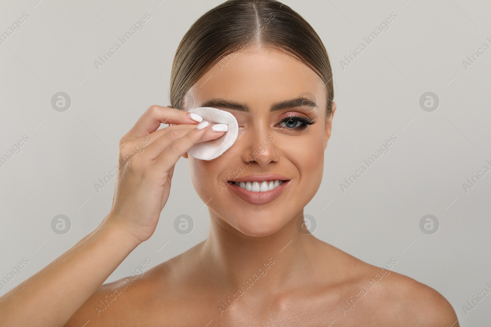 Photo of Beautiful woman removing makeup with cotton pad on light grey background