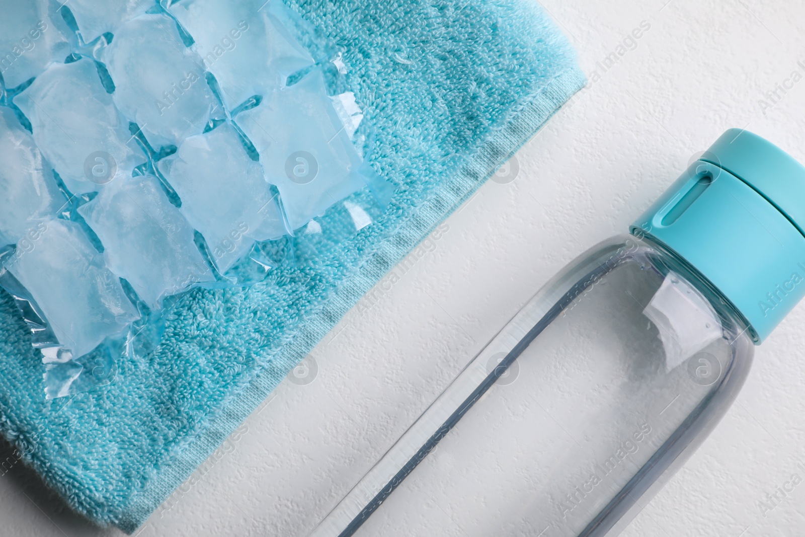 Photo of Bottle of water, ice pack and towel on white background, flat lay. Heat stroke treatment