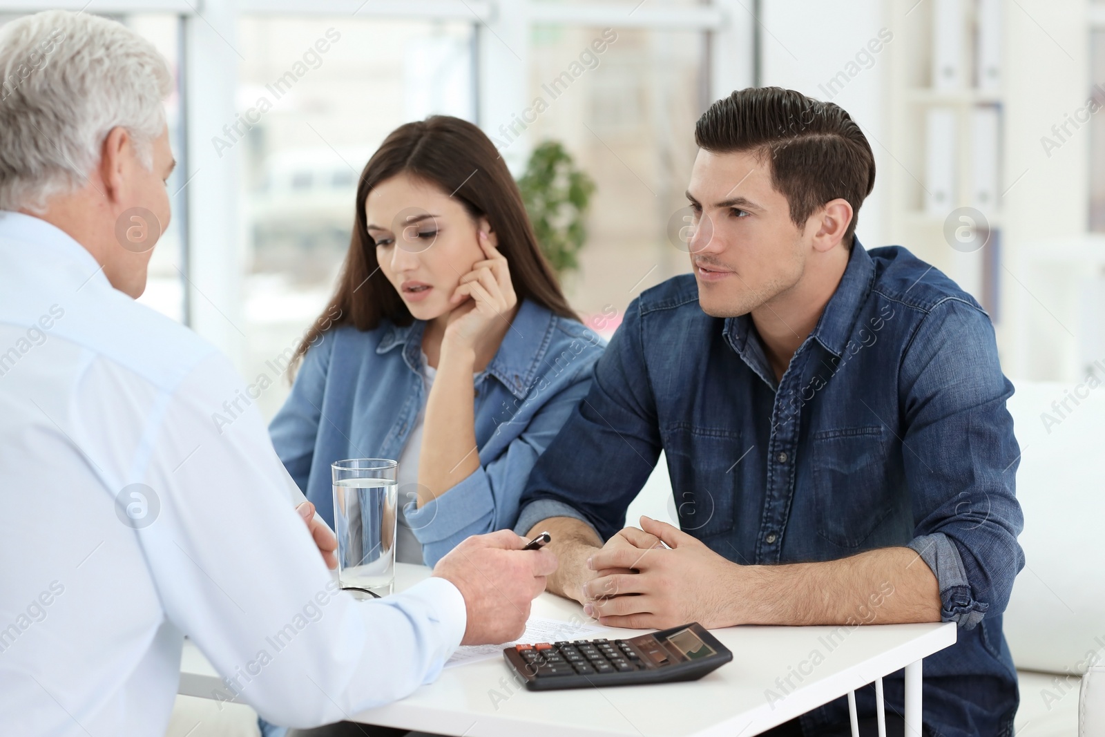 Photo of Young couple discussing pension plan with mature consultant in office
