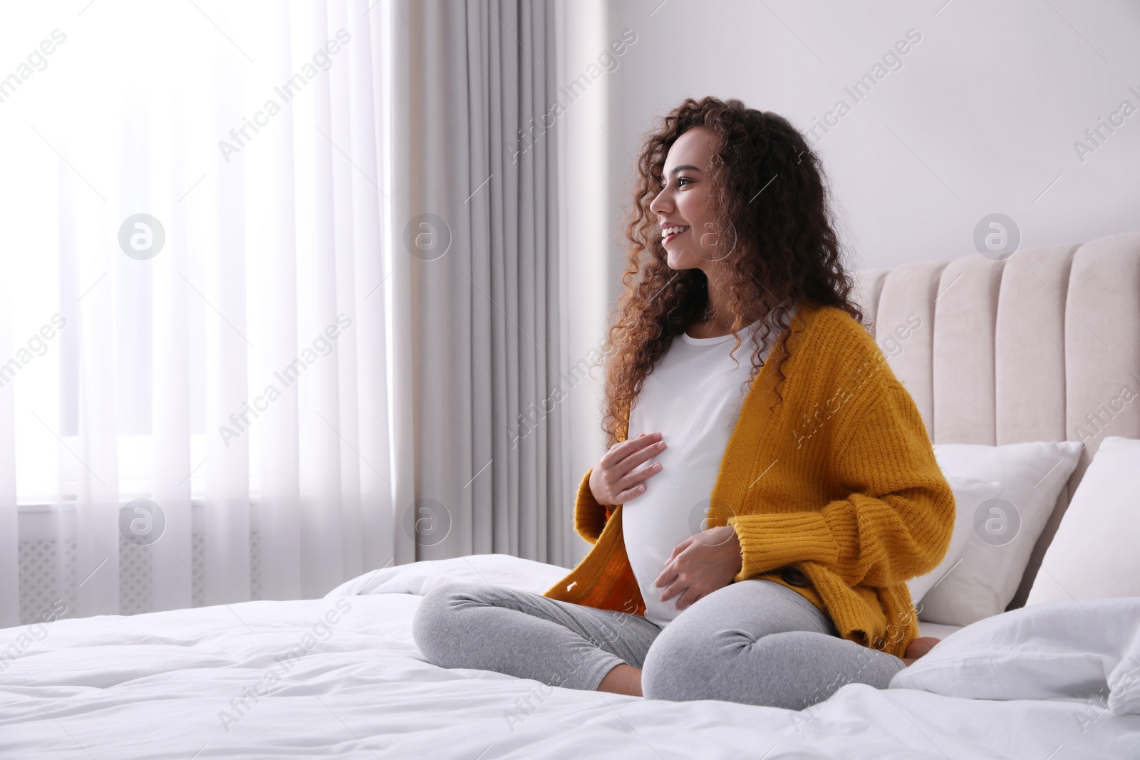 Photo of Pregnant young African-American woman sitting on bed at home