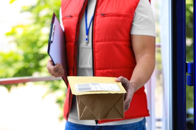 Photo of Young courier with parcels and clipboard on doorstep, closeup. Delivery service