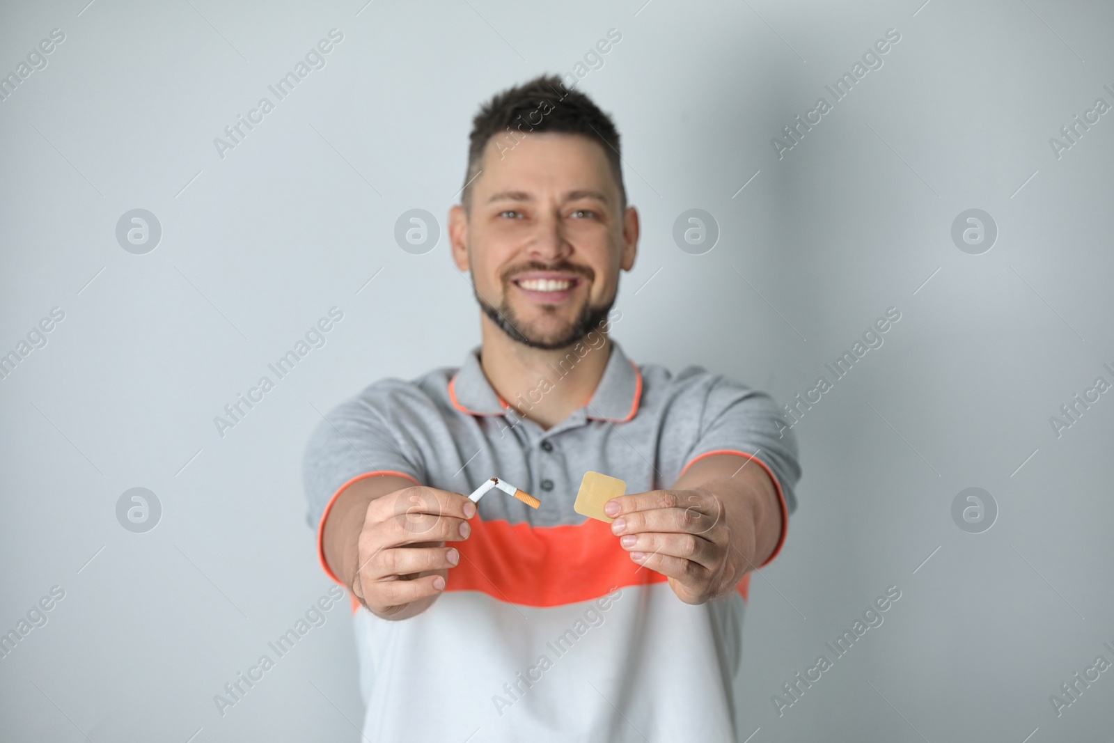 Photo of Happy man with nicotine patch and cigarette against light grey background, focus on hands