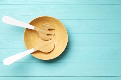 Fork and spatula in wooden bowl on light blue table, flat lay with space for text. Cooking utensils