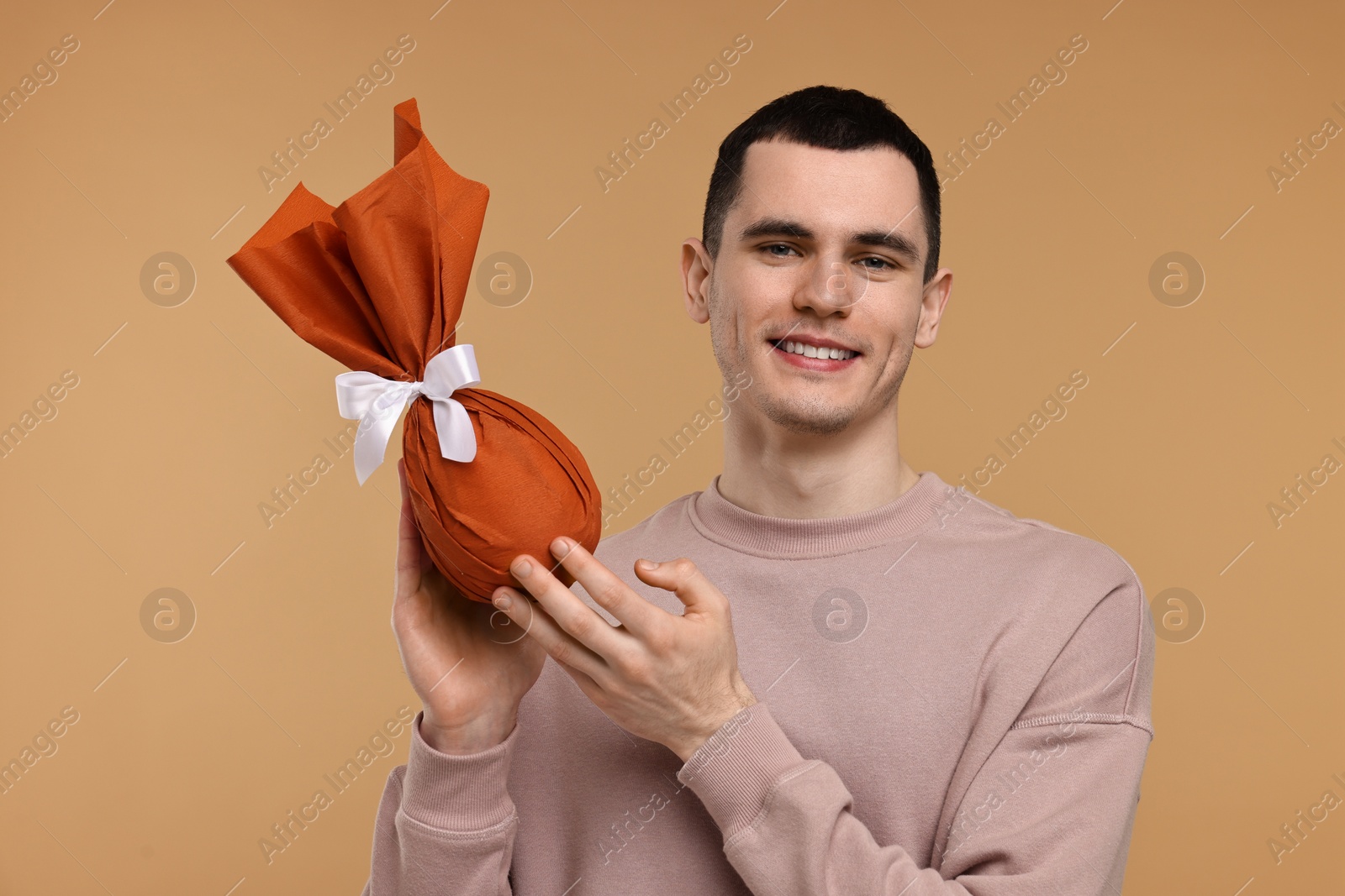 Photo of Easter celebration. Handsome young man with wrapped gift on beige background