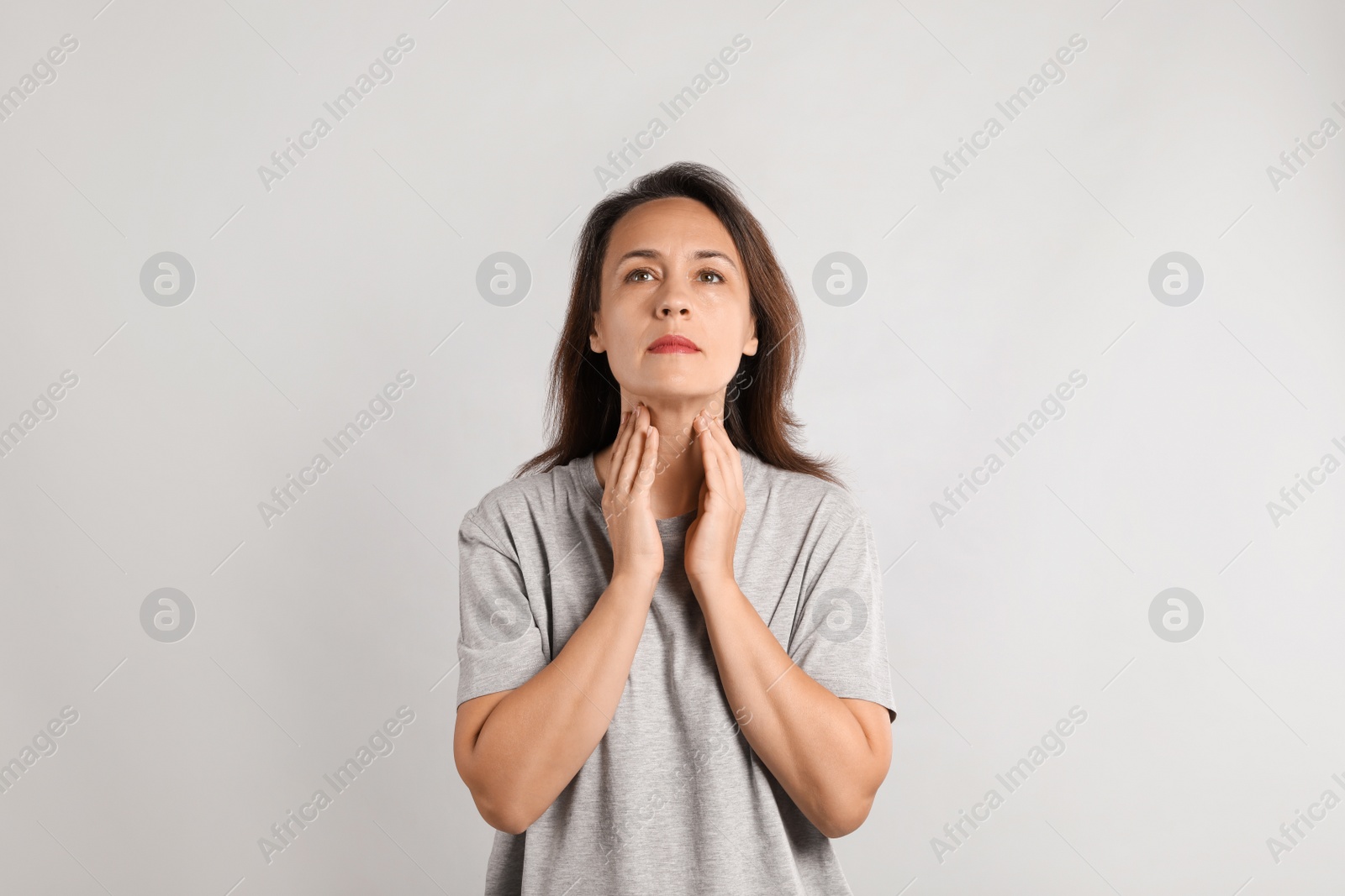 Photo of Mature woman doing thyroid self examination on light background