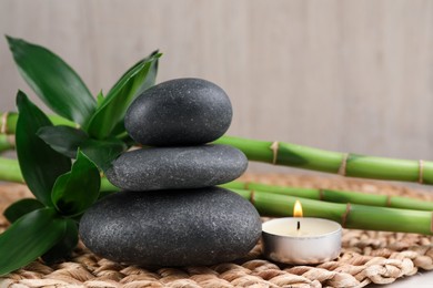 Photo of Stacked spa stones, bamboo and burning candle on wicker mat, closeup
