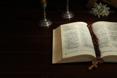 Photo of Cross, rosary beads, Bible and church candle on wooden table, space for text