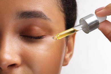 Woman applying serum onto her face on white background, closeup