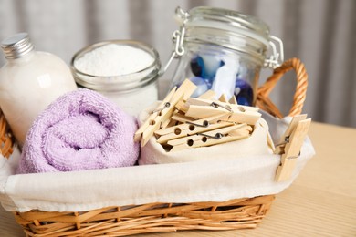 Wooden clothespins, towel and laundry detergents in wicker basket on table indoors, closeup