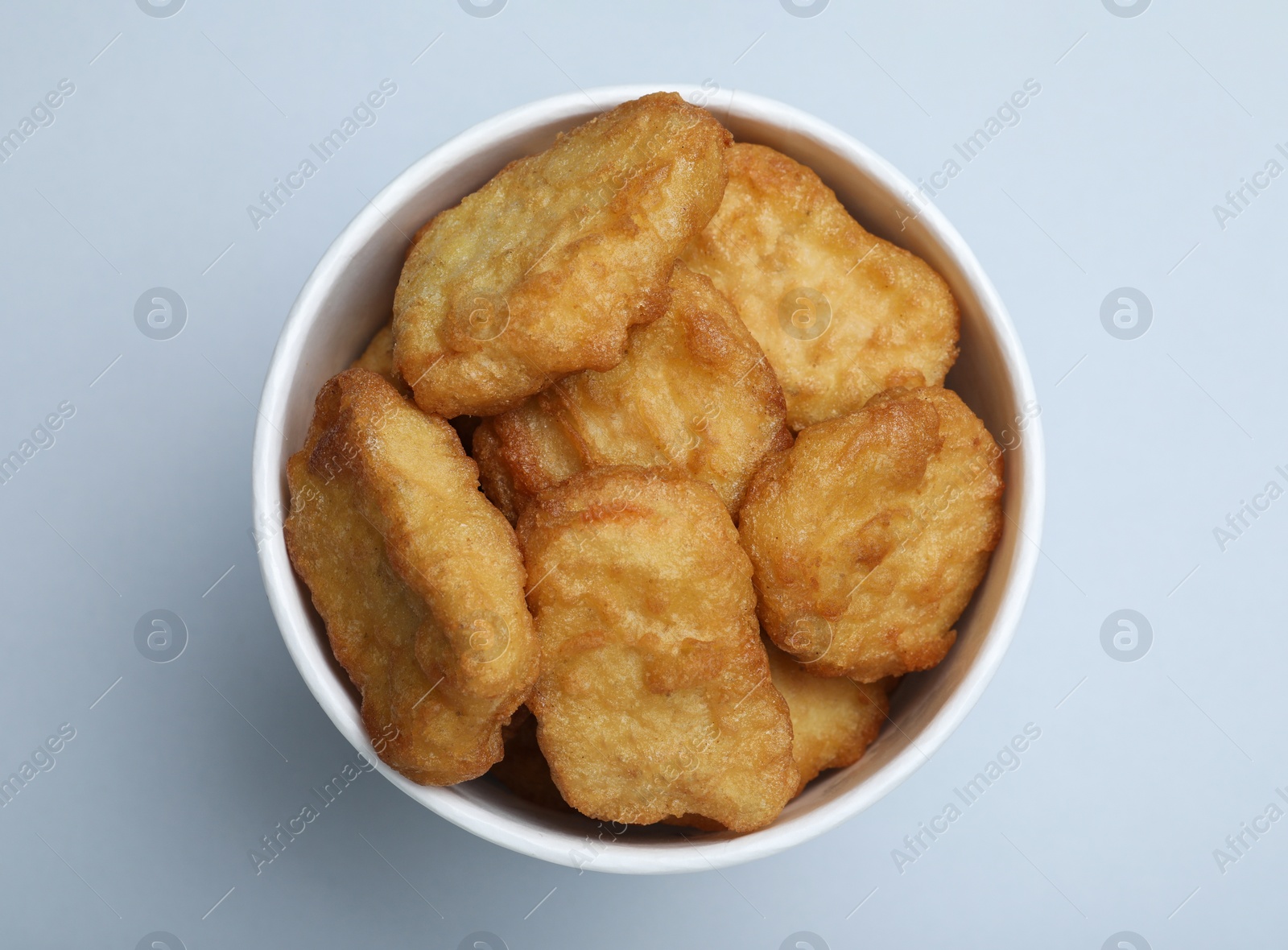 Photo of Bucket with delicious chicken nuggets on light background, top view