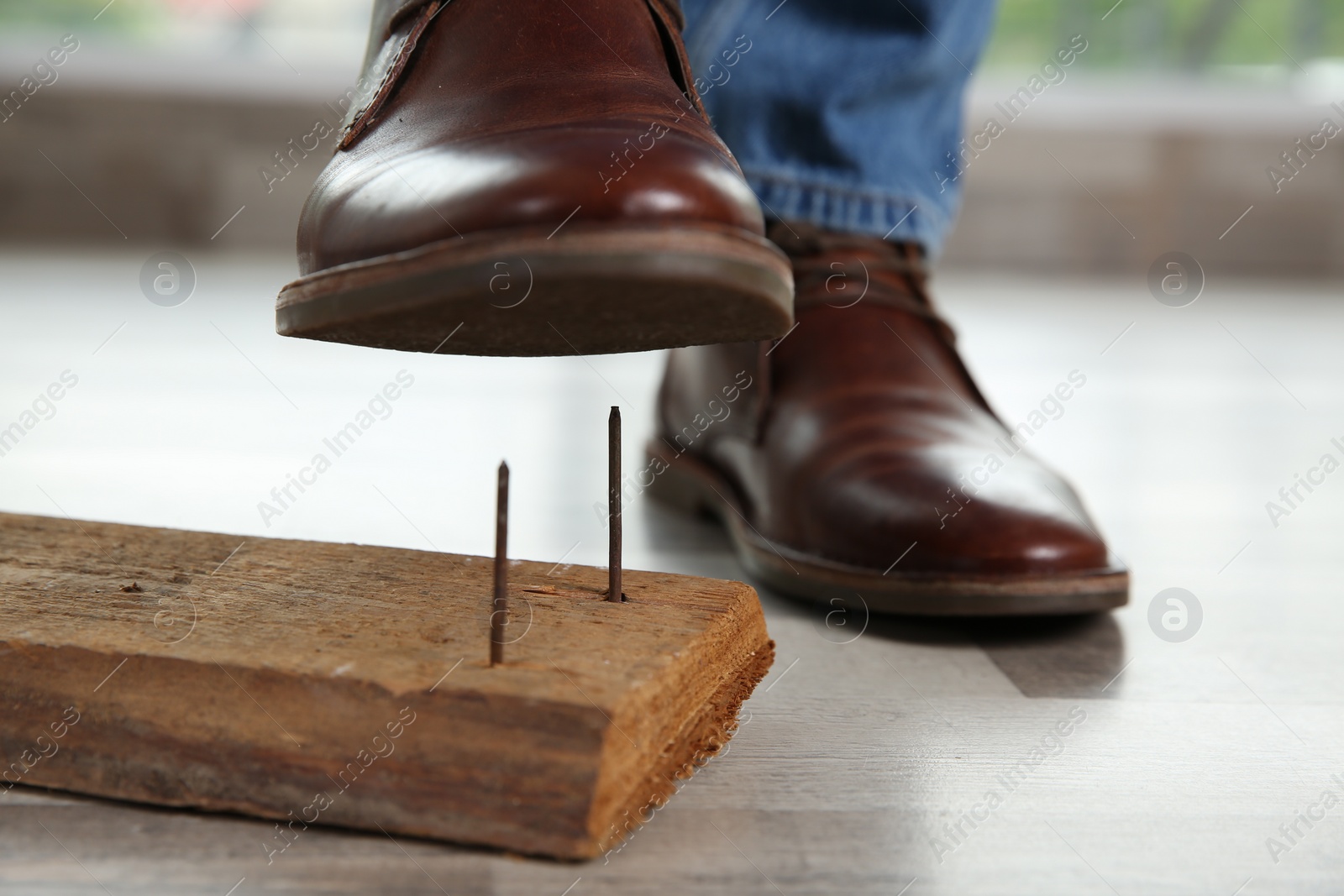 Photo of Careless man stepping on nails in wooden plank, closeup