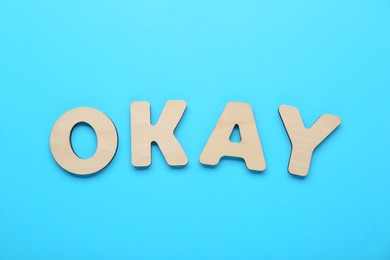 Word Okay made of wooden letters on light blue background, top view