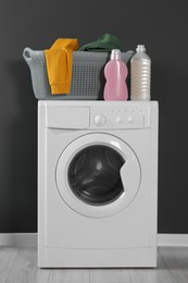 Photo of Washing machine with clothes and detergents near black wall indoors. Interior design