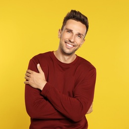 Photo of Happy young man in sweatshirt on yellow background. Winter season