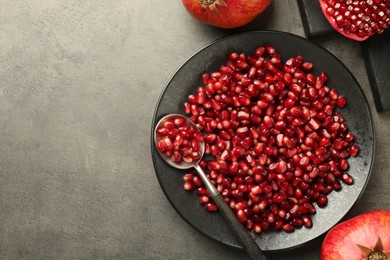 Photo of Ripe juicy pomegranate grains on grey textured table, flat lay. Space for text