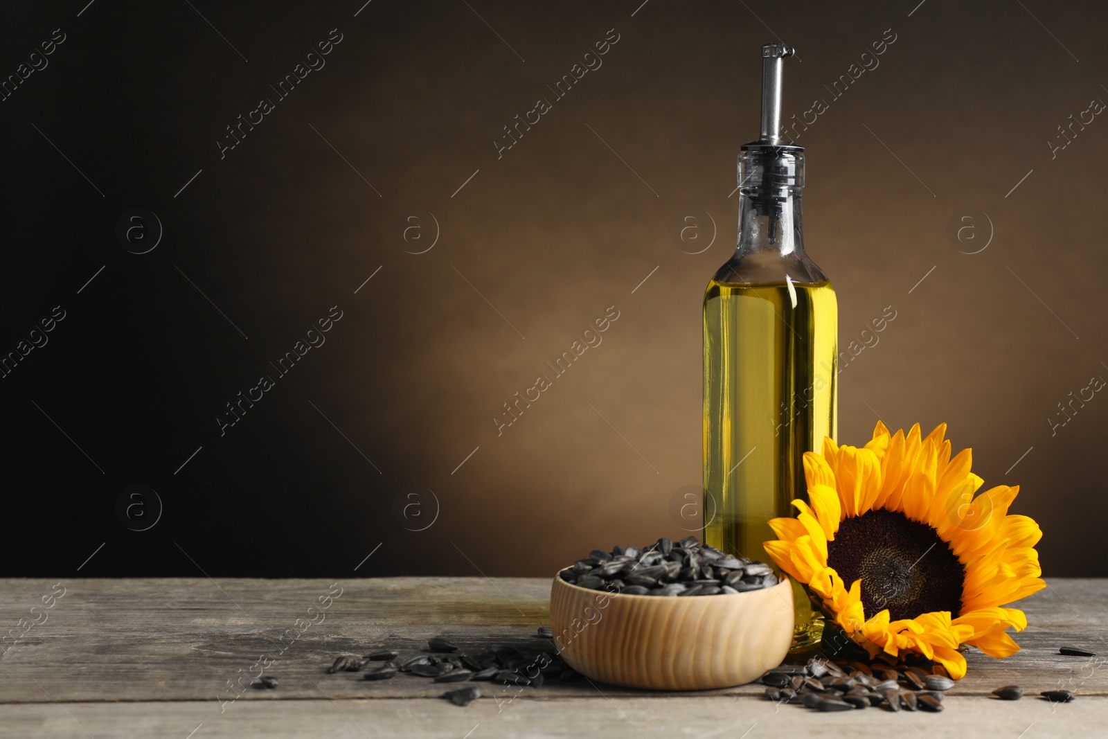 Photo of Sunflower cooking oil, seeds and yellow flower on light grey table, space for text