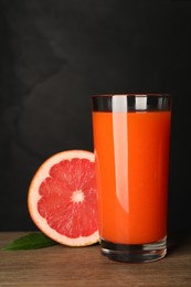 Photo of Tasty grapefruit juice in glass, leaf and fresh fruit on wooden table against black background