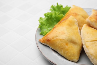 Delicious samosas and lettuce on white tiled table, closeup. Space for text