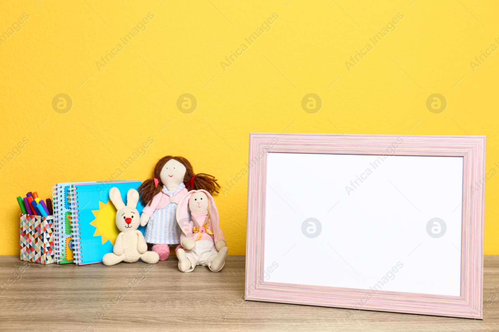 Photo of Soft toys and photo frame on table against yellow background, space for text. Child room interior