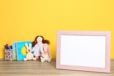 Soft toys and photo frame on table against yellow background, space for text. Child room interior