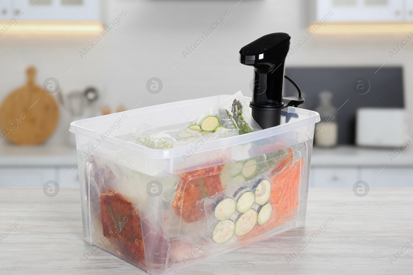 Image of Sous vide cooker and vacuum packed food products in box on wooden table in kitchen. Thermal immersion circulator