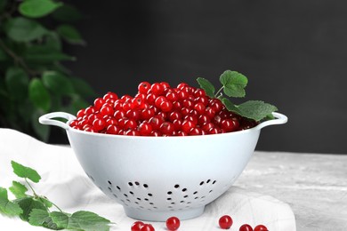 Ripe red currants and leaves in colander on table