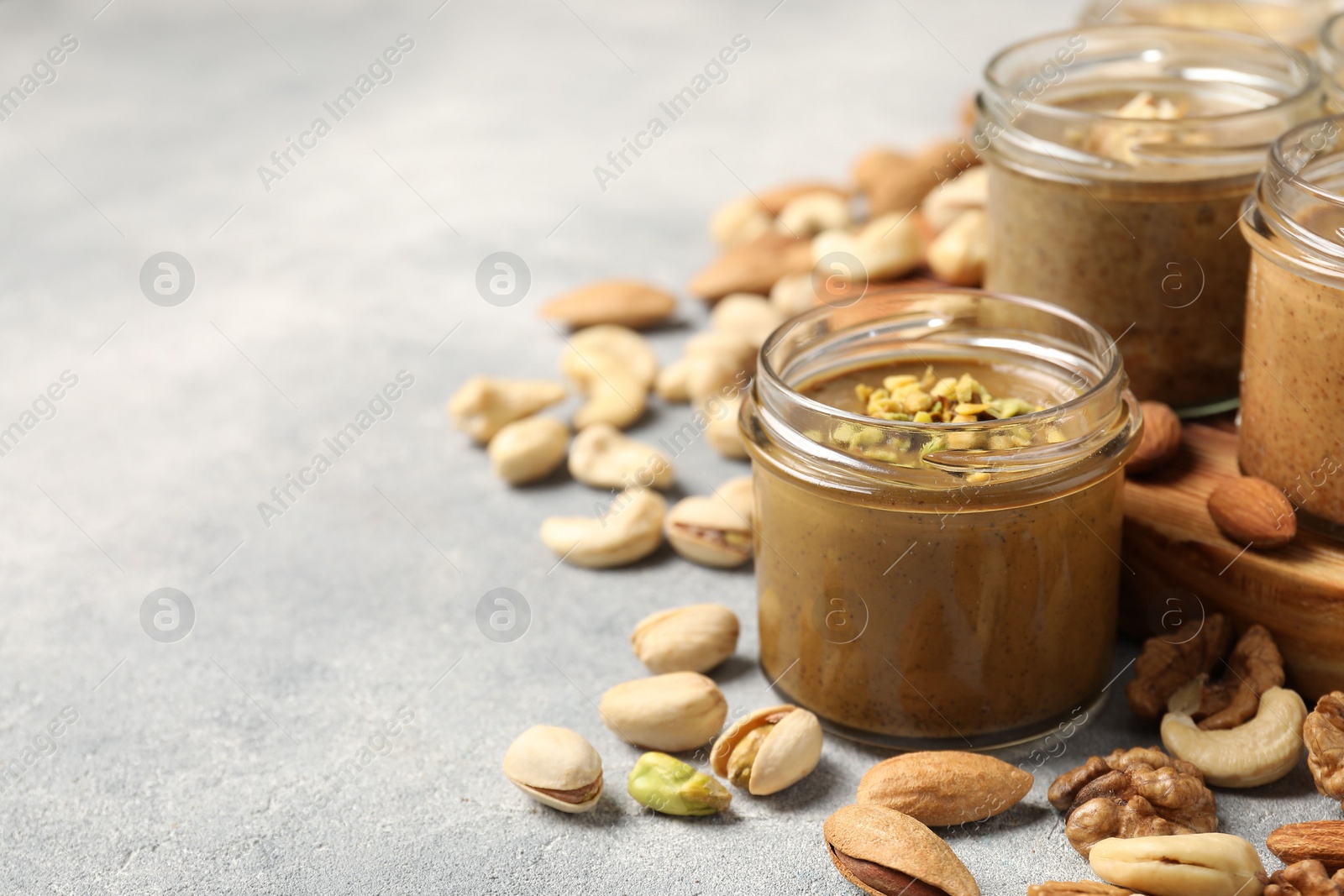 Photo of Tasty nut butters in jars and raw nuts on light grey table, space for text