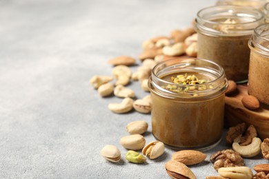 Tasty nut butters in jars and raw nuts on light grey table, space for text