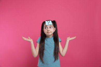 Photo of Confused girl with question mark sticker on forehead against pink background