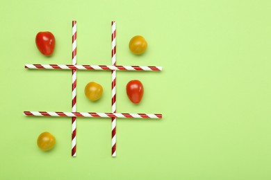 Photo of Tic tac toe game made with cherry tomatoes on light green background, top view