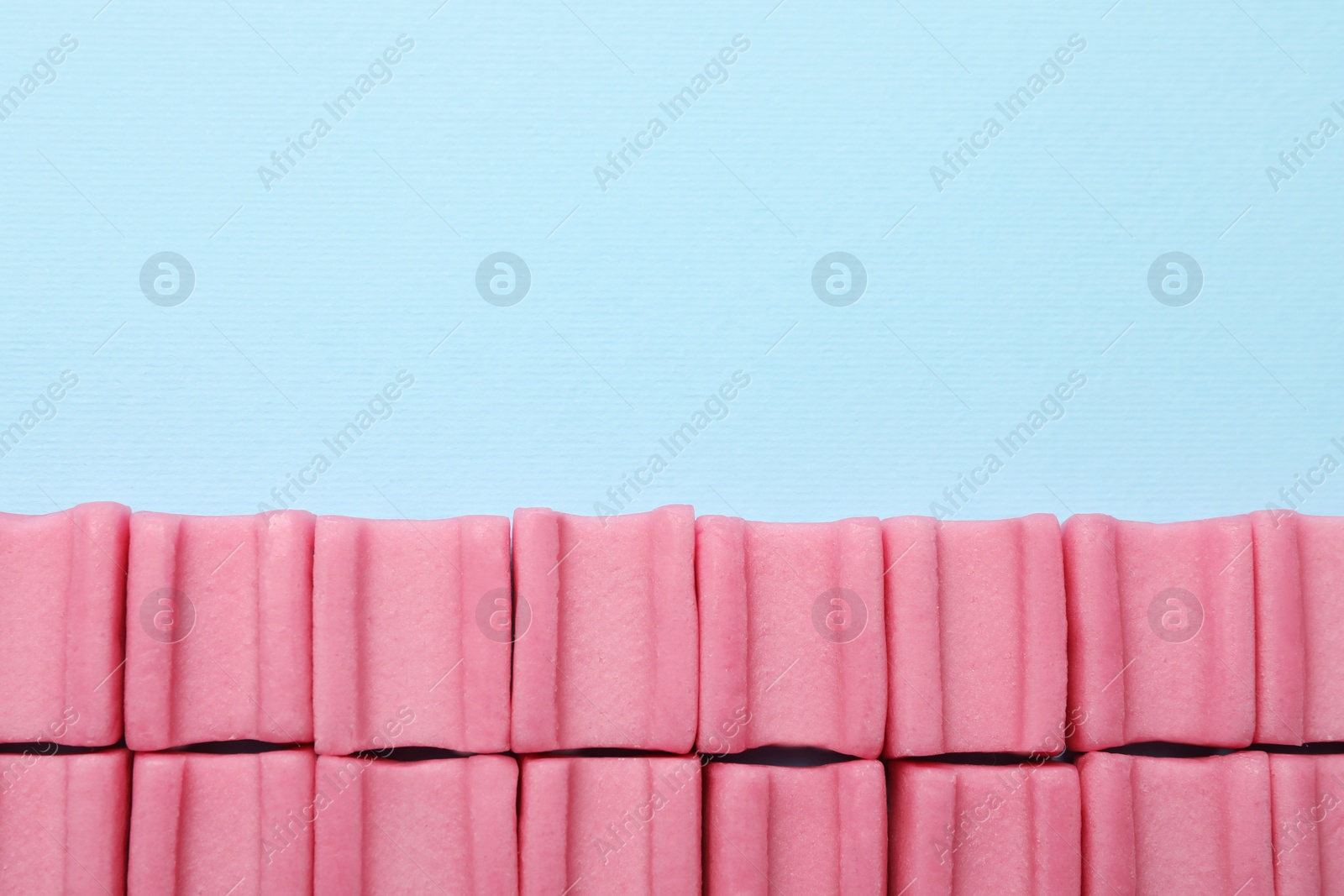 Photo of Tasty pink chewing gums on light blue background, flat lay. Space for text