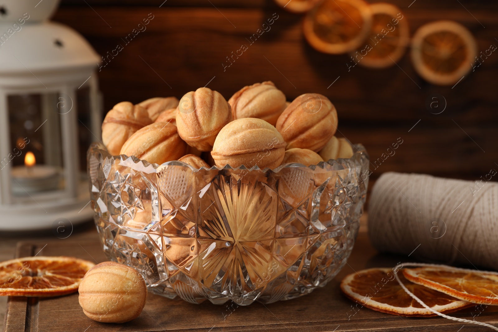 Photo of Bowl of delicious nut shaped cookies and dried orange slices on wooden table, closeup