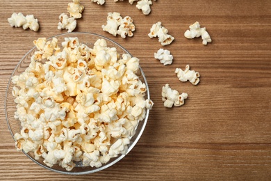 Glass bowl with tasty popcorn on wooden background, top view. Space for text