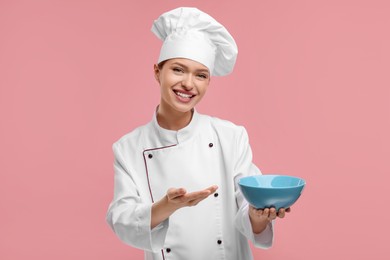 Photo of Happy chef in uniform holding bowl on pink background