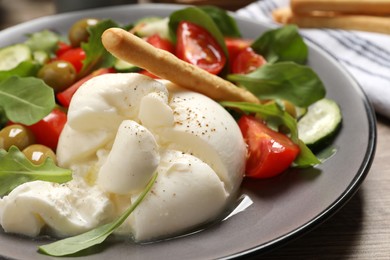 Photo of Delicious burrata salad served on wooden table, closeup