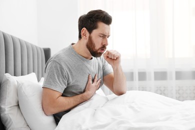 Photo of Sick man coughing on bed at home. Cold symptoms