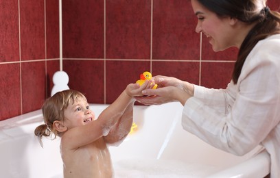 Happy mother playing with her little daughter in bathroom