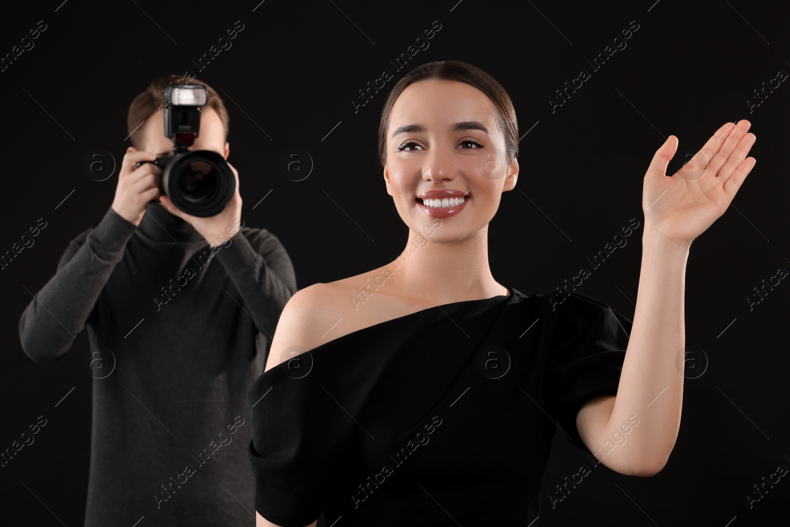 Photo of Photographer taking picture of beautiful woman on black background, selective focus