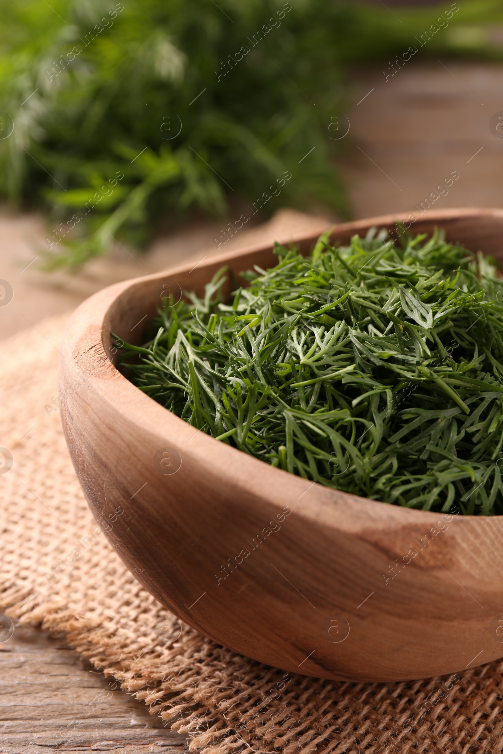 Photo of Fresh cut dill in bowl on wooden table, closeup