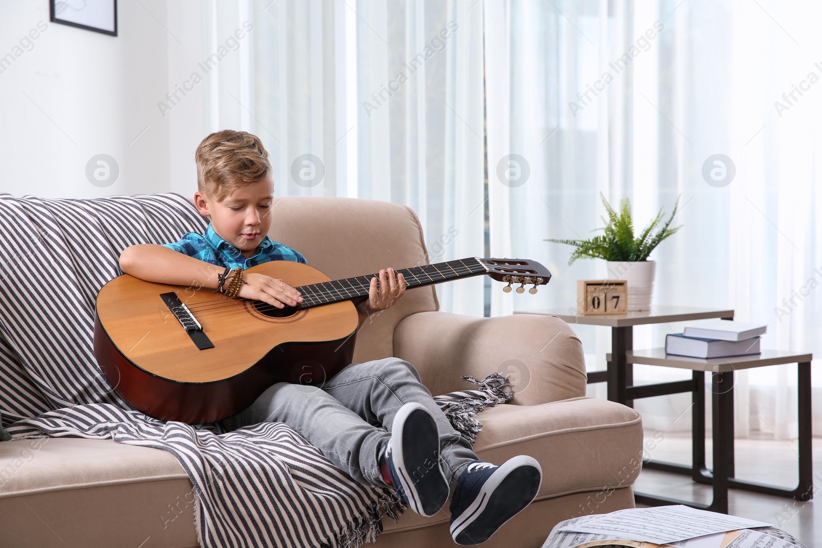 Photo of Cute little boy playing guitar on sofa in room