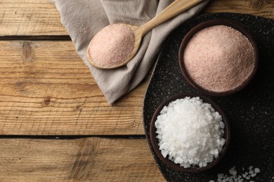 Photo of Different natural salt on wooden table, flat lay. Space for text