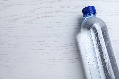 Photo of Plastic bottle with water on white wooden background, top view. Space for text