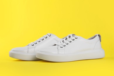 Photo of Pair of stylish white sneakers on yellow background