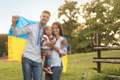 Photo of Happy cute family in embroidered national shirts with Ukrainian flag on sunny day. Space for text