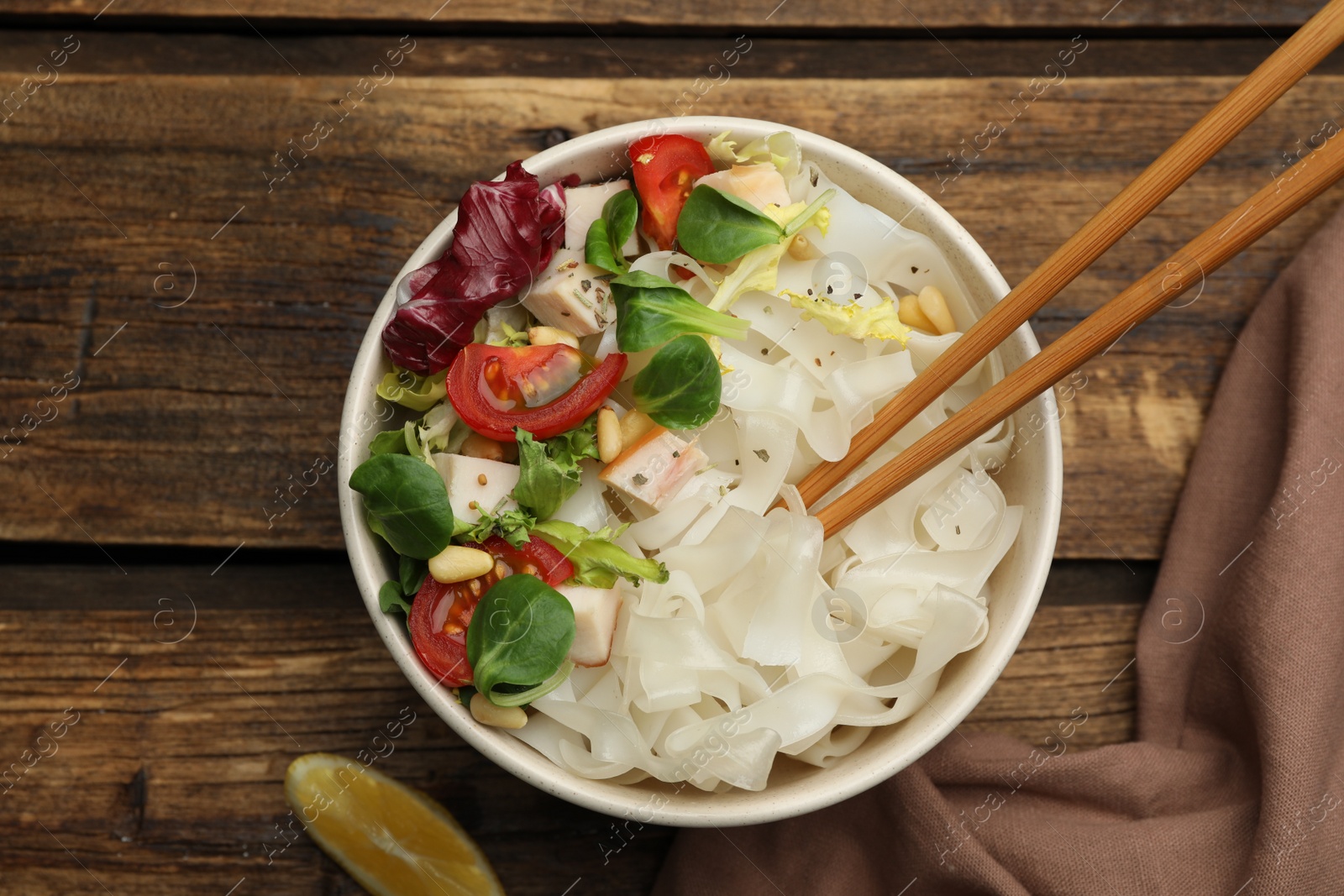 Photo of Tasty cooked rice noodles with chicken and vegetables on wooden table, flat lay