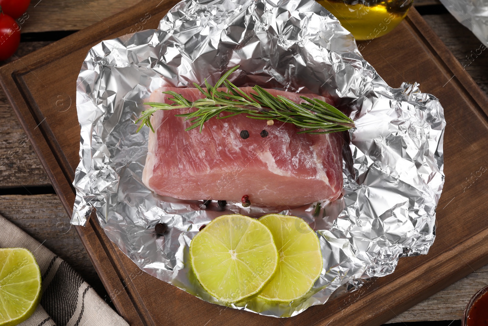 Photo of Aluminum foil with raw meat, rosemary, lime and spices on wooden table, above view