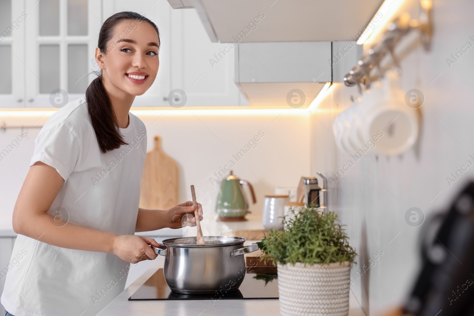 Photo of Smiling woman cooking soup in light kitchen