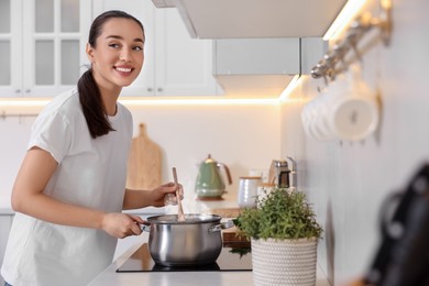 Smiling woman cooking soup in light kitchen